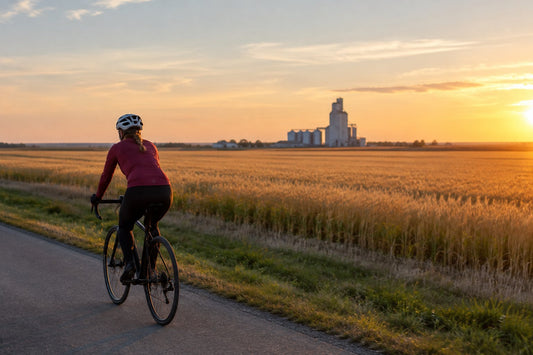 Cyclist wearing a properly fitted bike helmet riding along a quiet paved path beside the Prairie fields in Canada on a clear summer evening